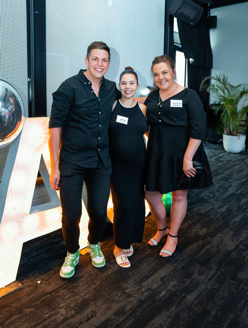 Three event staff members wearing black outfits pose together at a venue with an illuminated decor piece on a dark floor.