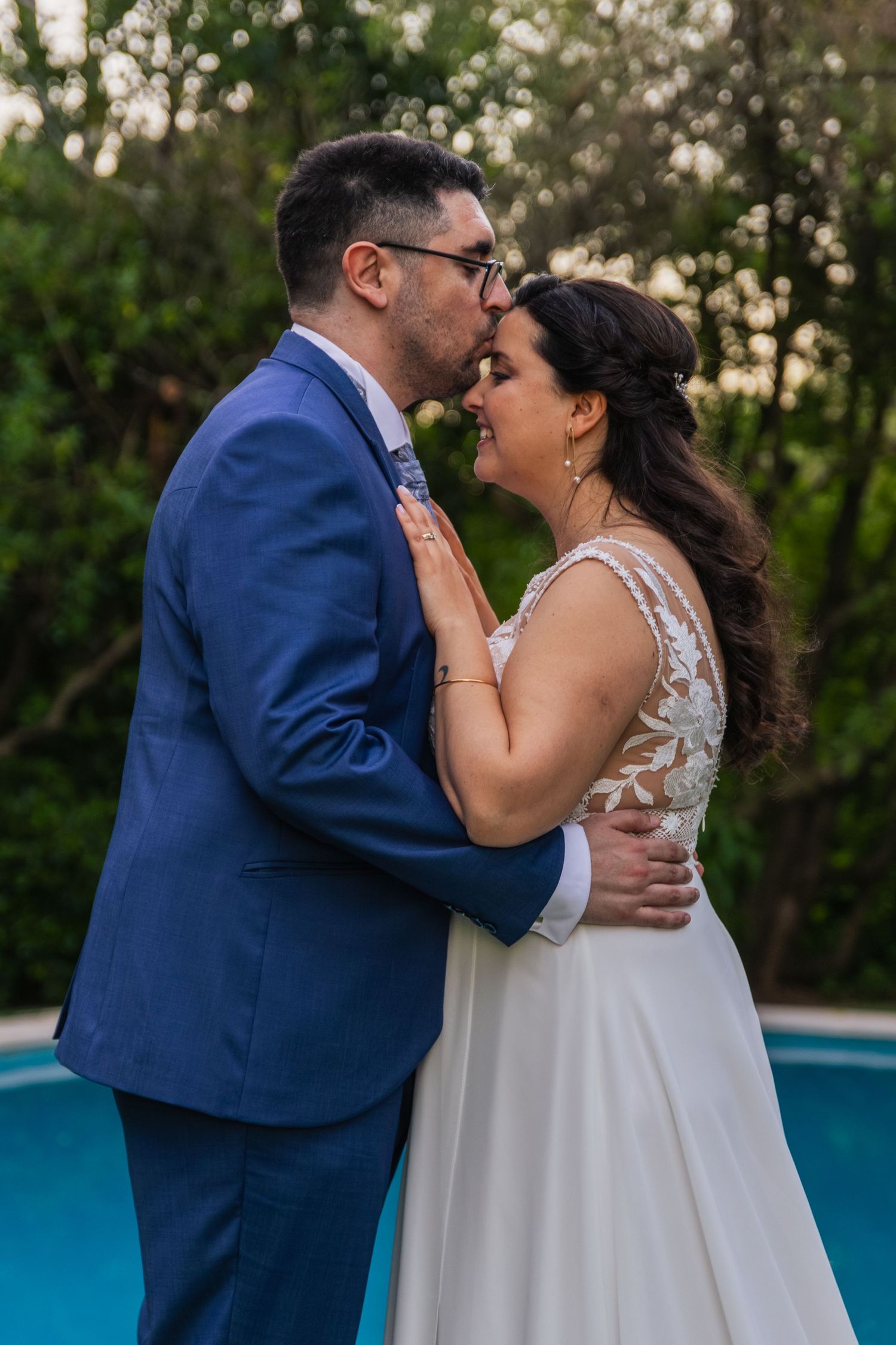 Romantic moment between couple by poolside during sunset wedding celebration.