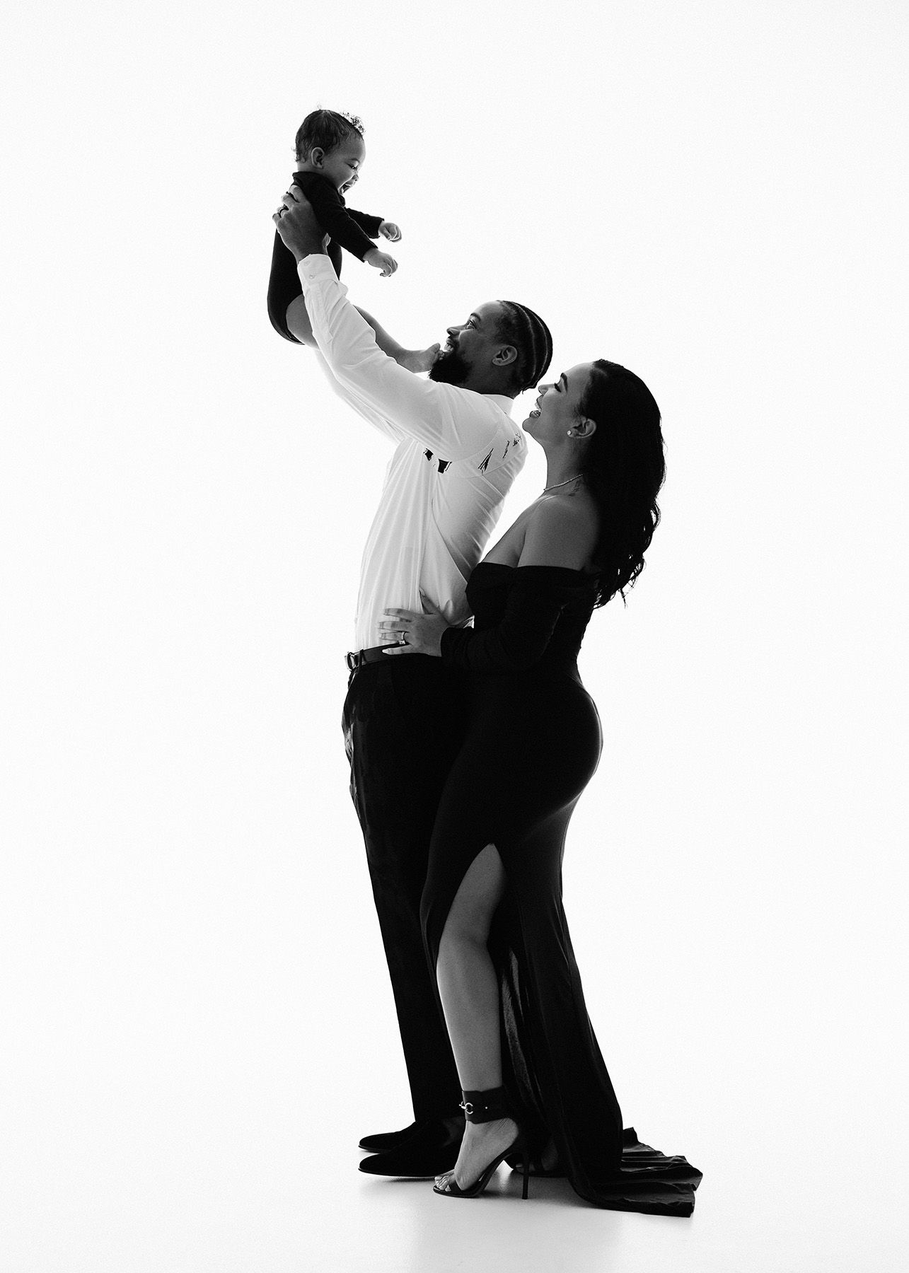 Elegant black and white portrait of couple in formal attire striking an intimate dance pose against plain backdrop.