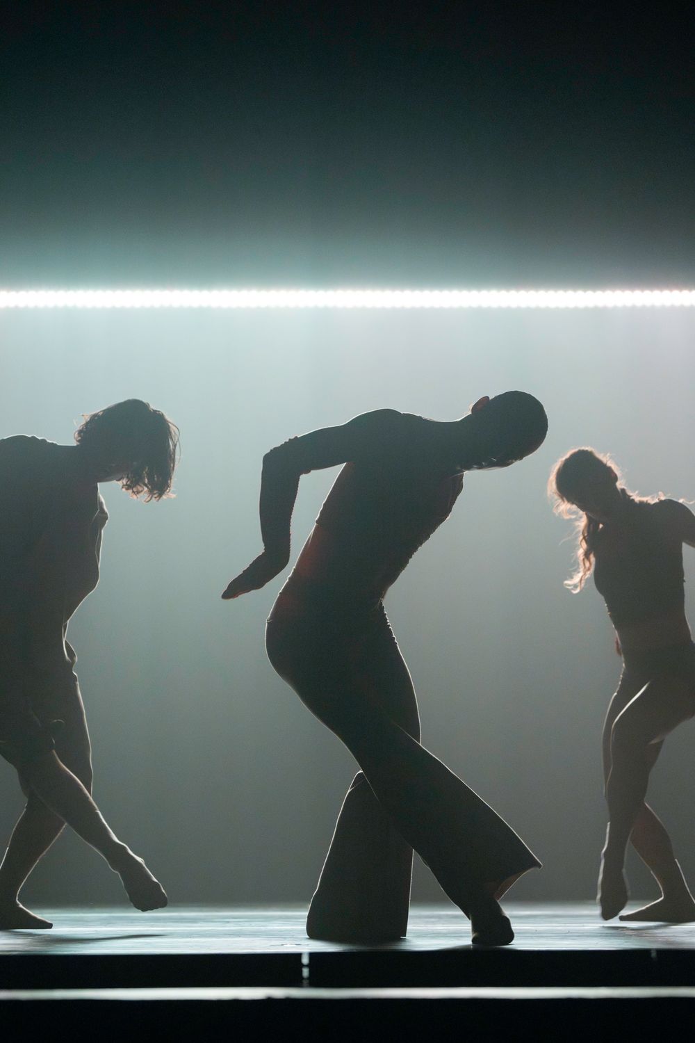 Silhouettes of dancers performing on stage with dramatic backlight and moody atmospheric lighting effects.