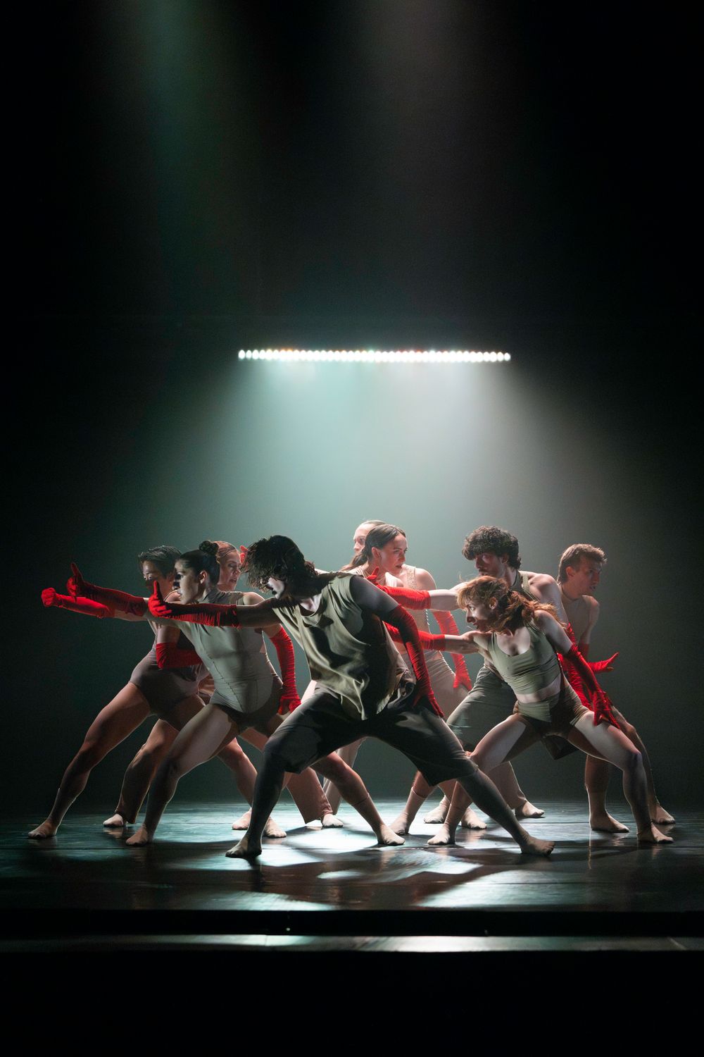 Modern dance ensemble performing in dramatic lighting as they move in synchronized formation on stage.