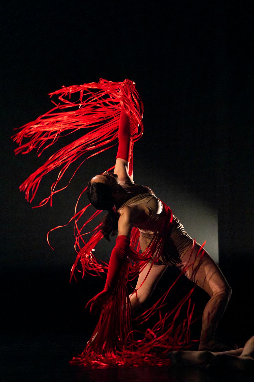 A contemporary dancer performs with flowing red fabric in a dark theatrical setting.