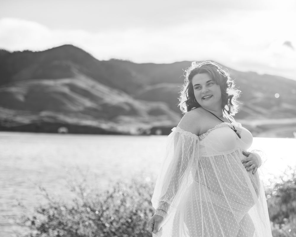 A joyful figure in a flowing white lace dress poses outdoors against a mountainous backdrop in black and white.