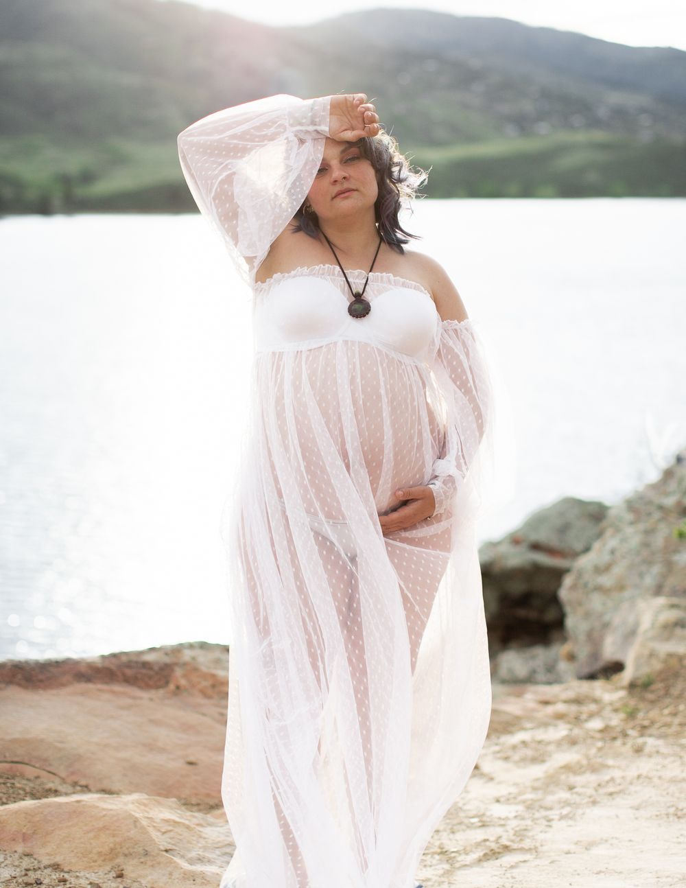Ethereal figure in flowing sheer white fabric poses gracefully against a misty lakeside mountain landscape.