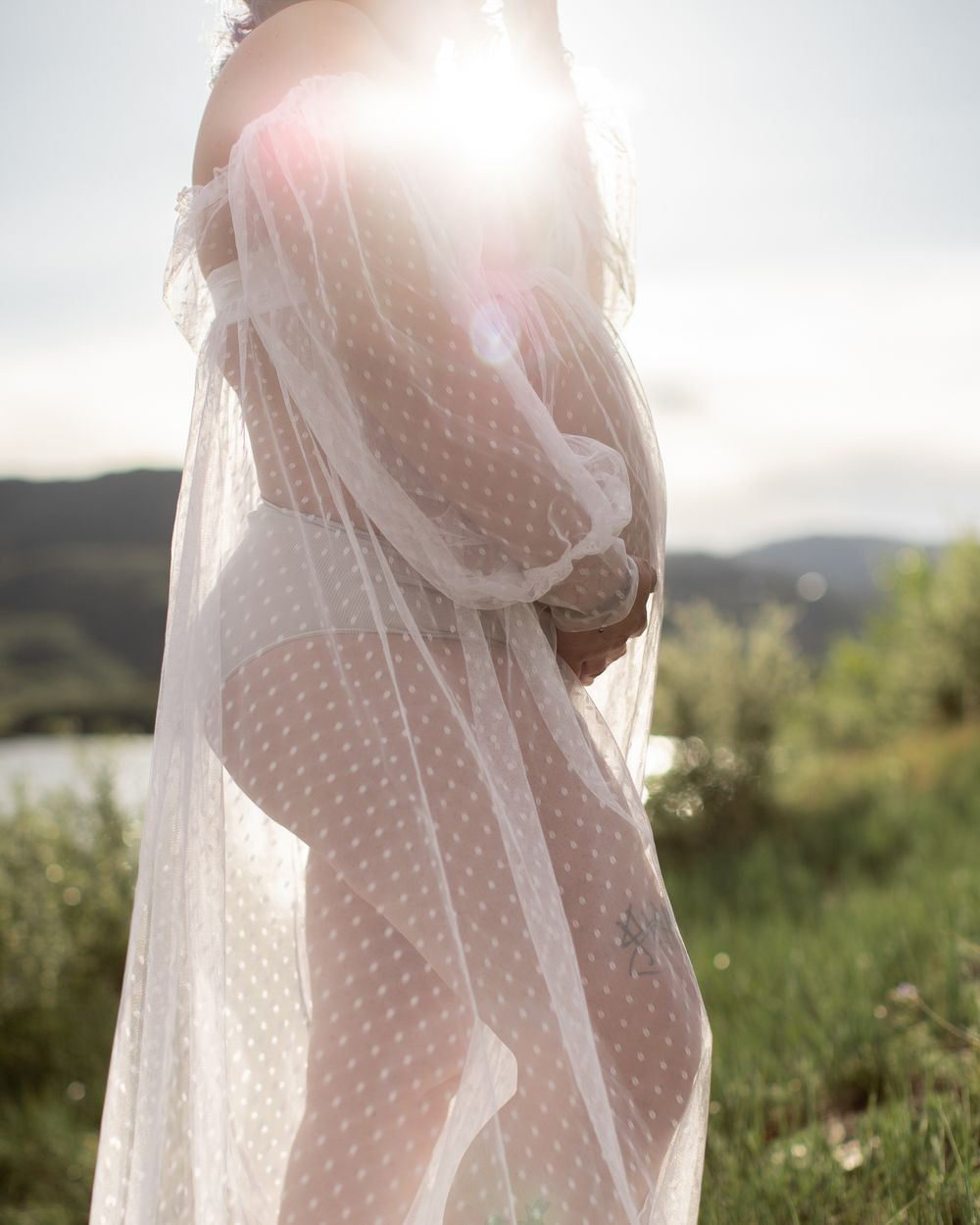 Ethereal bridal portrait silhouetted against sunlight wearing a delicate polka dot veil in a natural outdoor setting.