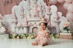 Pink castle backdrop with floral decorations and balloons creates a dreamy princess-themed setting.