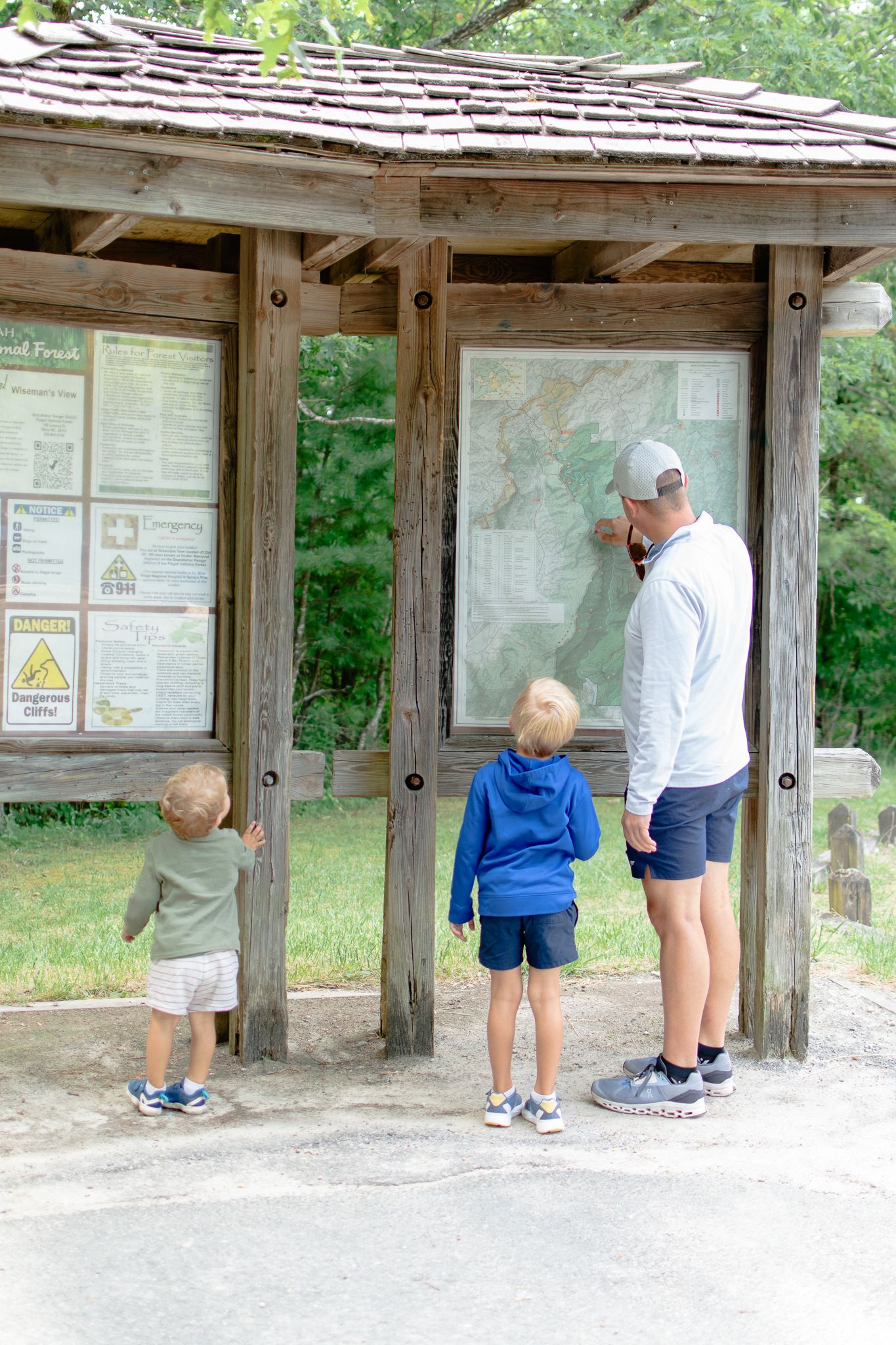 Adult and child observe information posted on a wooden bulletin board at a trail's information kiosk.