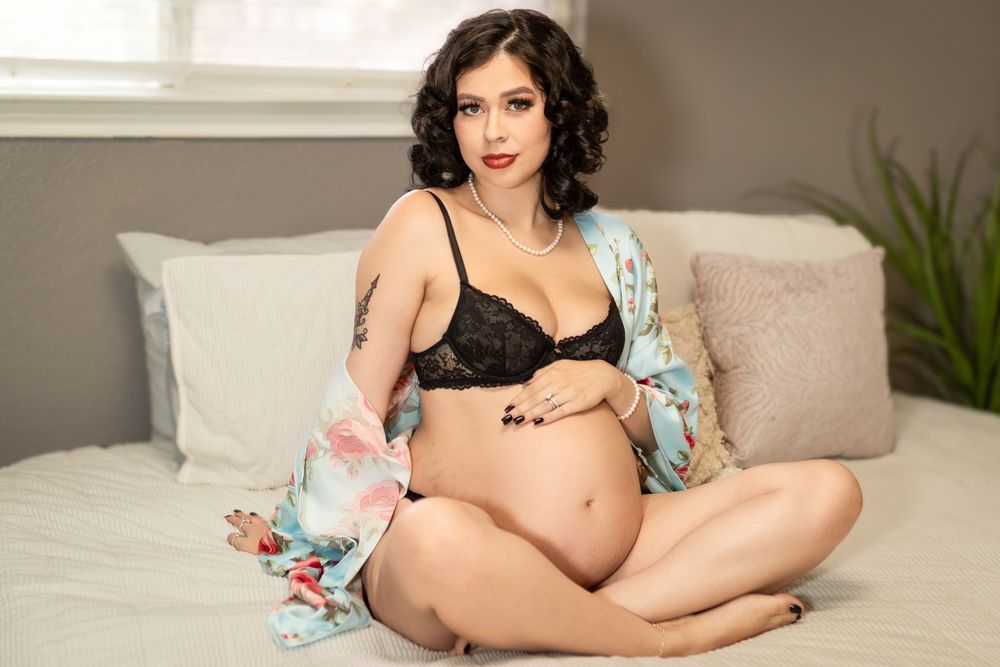 During a fort worth maternity boudoir session, an expecting mother sits cross-legged on a luxurious bed in Fort Worth.