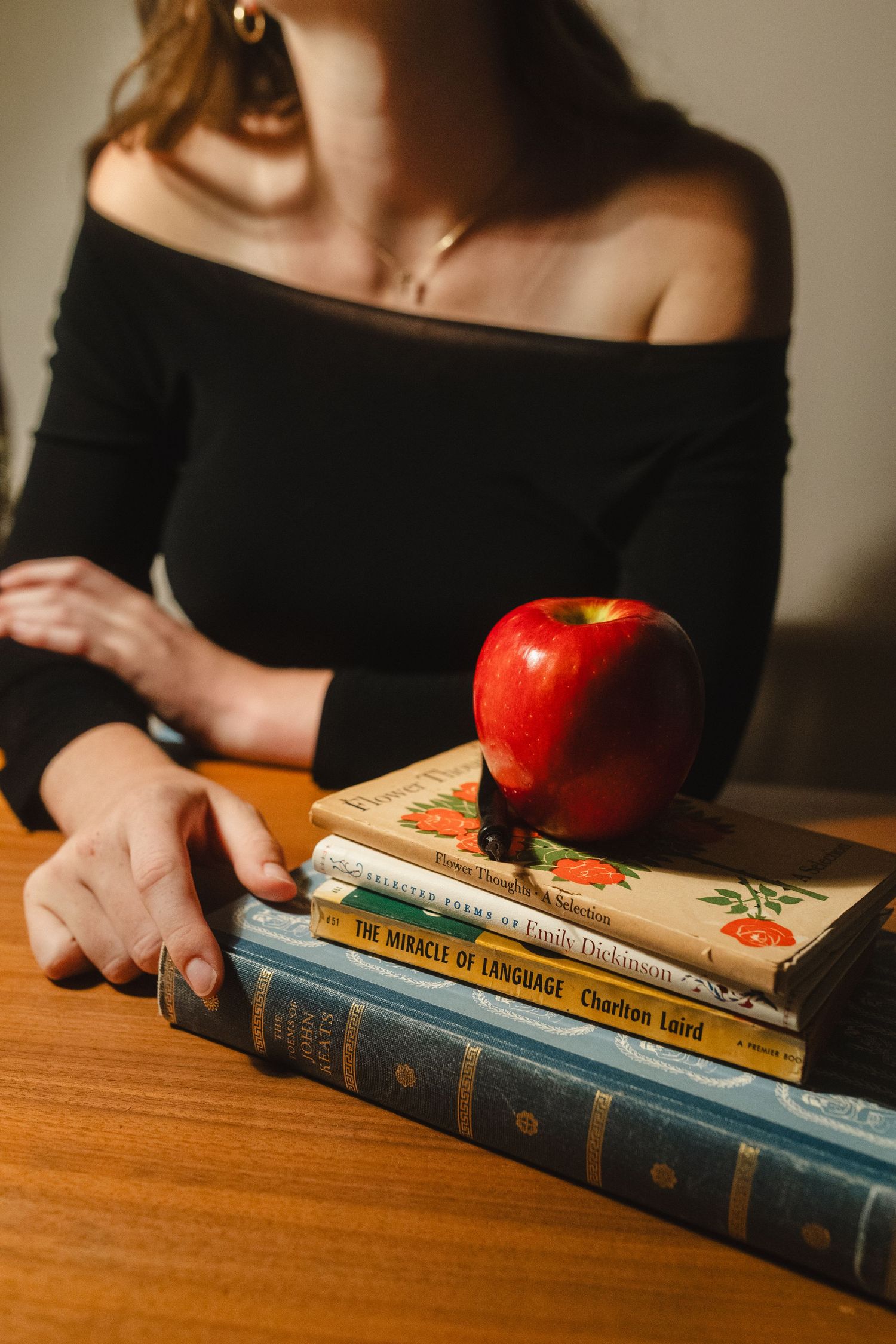 Still life with red apple and stack of vintage books on wooden table.