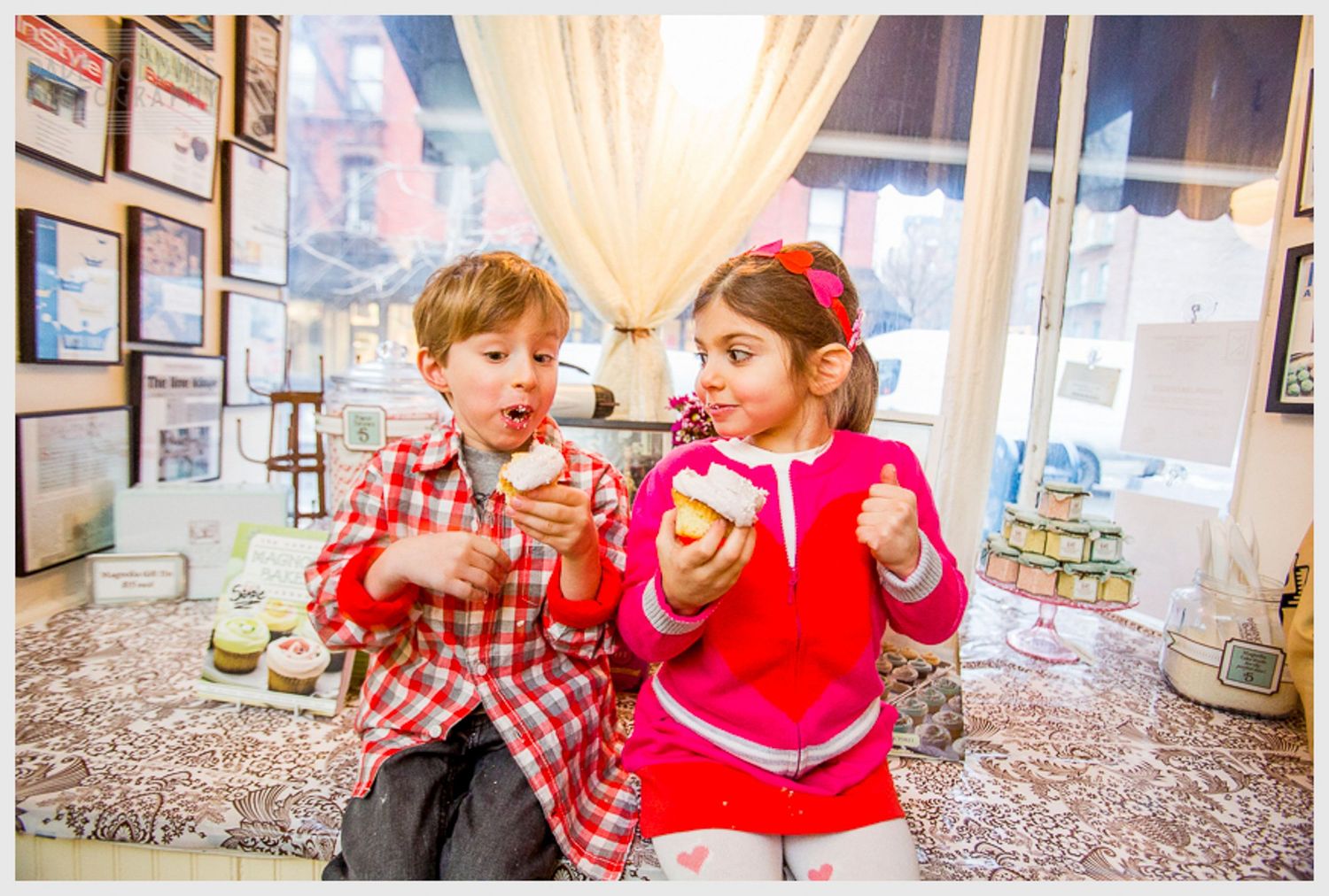 Children enjoying treats at cafe table with urban view through window.