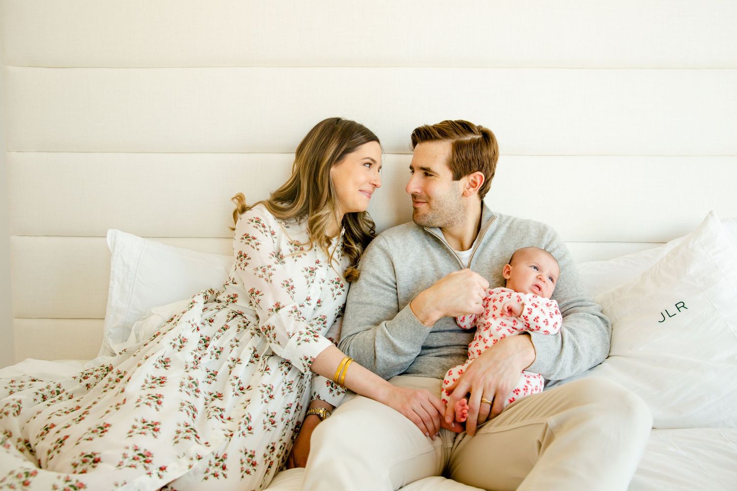 A tender family moment of new parents cuddling with their baby on a white bed.