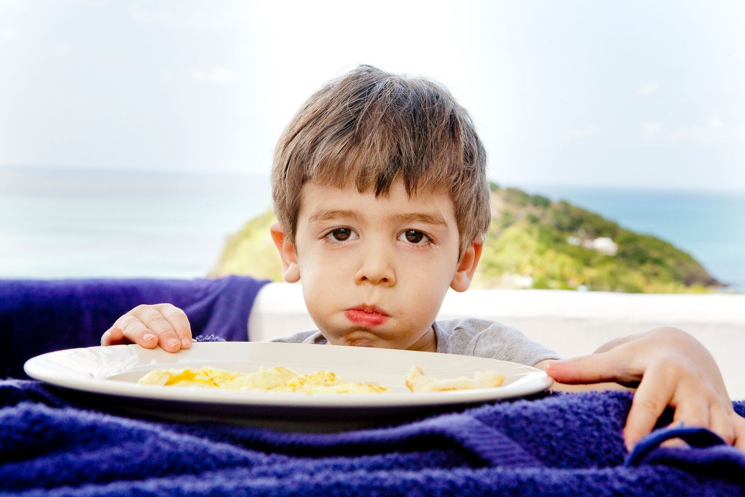 A youngster rests head on plate while looking at camera with pouty expression.