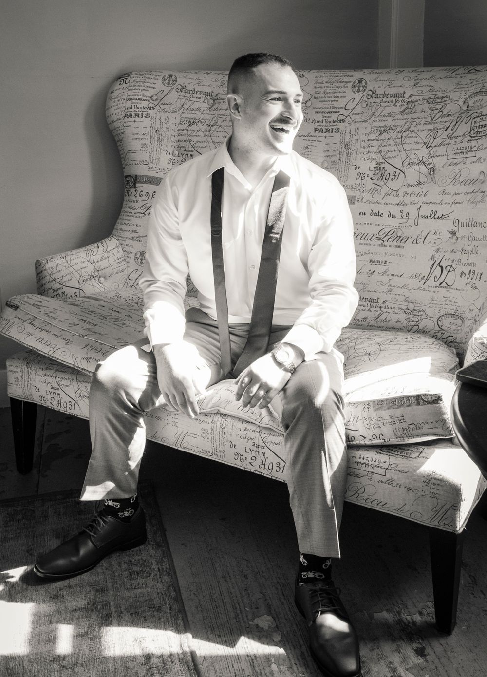 Black and white photos of wedding preparations on a vintage patterned couch with natural lighting.