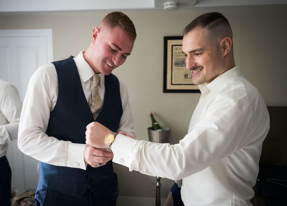 Wedding preparation scene showing formal attire adjustments in a softly lit room.
