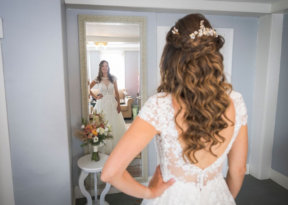 A wedding dress with intricate lace detailing and flowing curled hairstyle adorned with floral accessories.