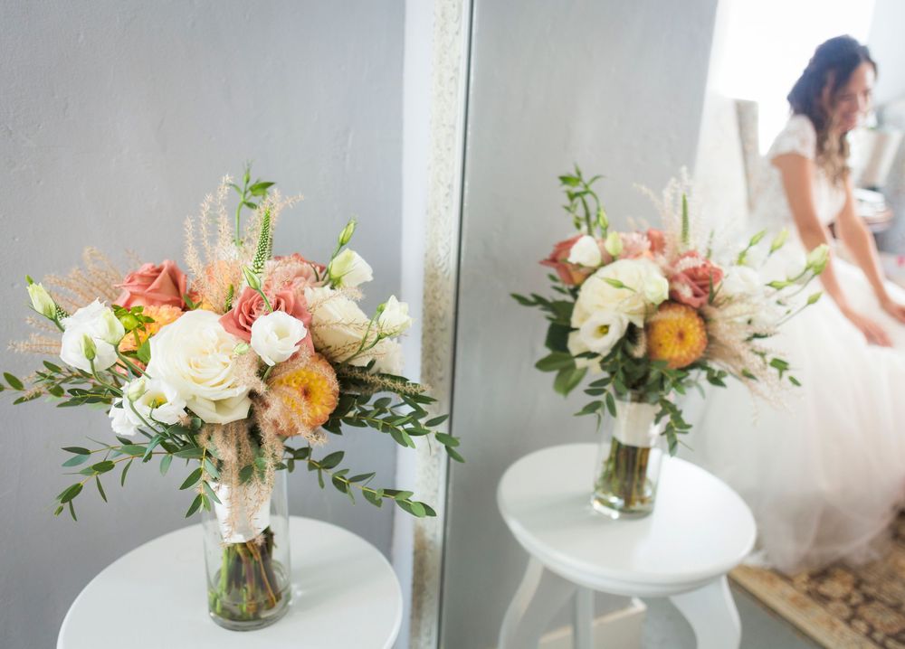 Elegant wedding bouquet with roses and greenery sits on white table with mirror reflection.
