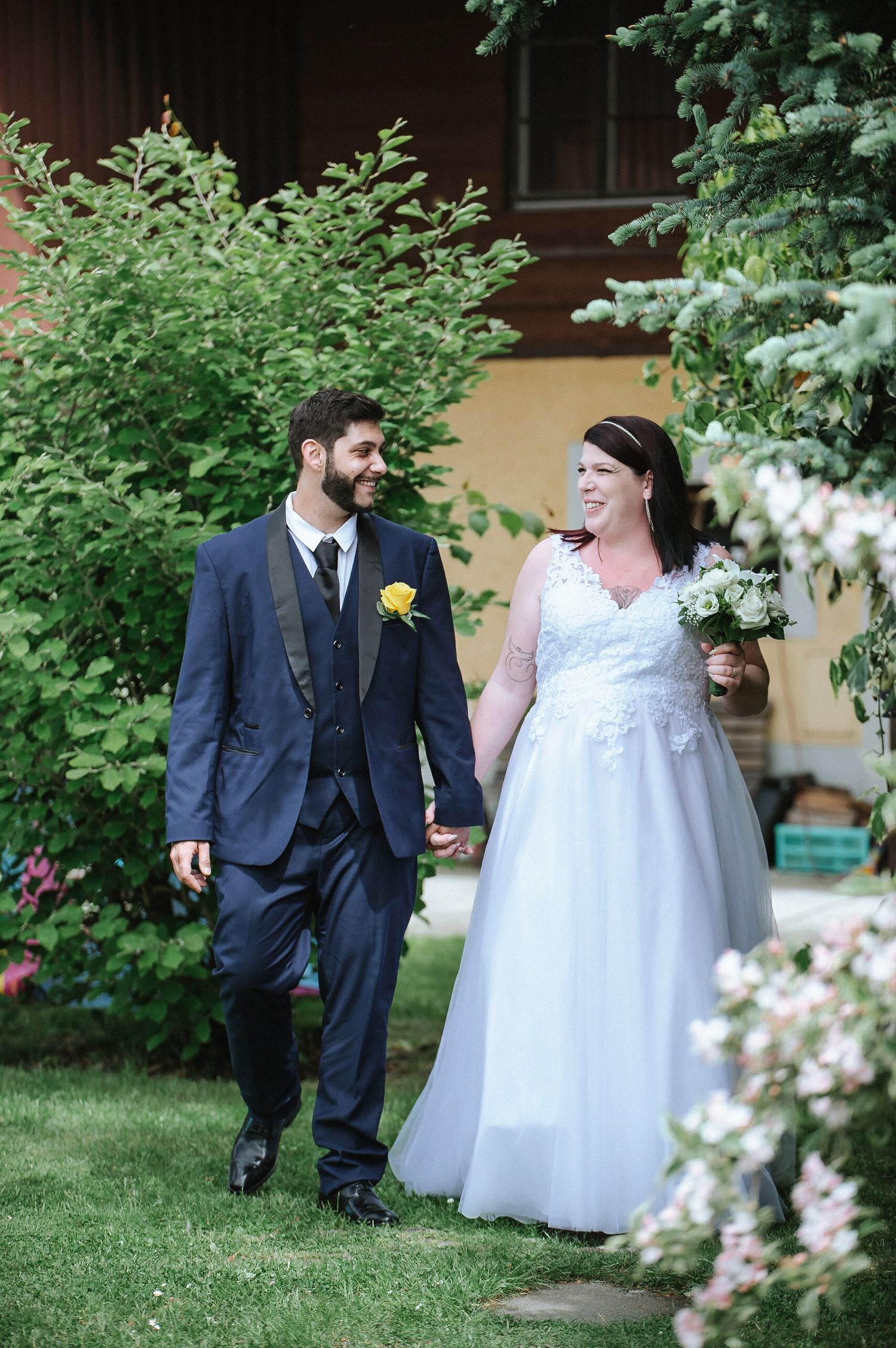 A wedding couple shares a romantic moment among blooming garden flowers and greenery.