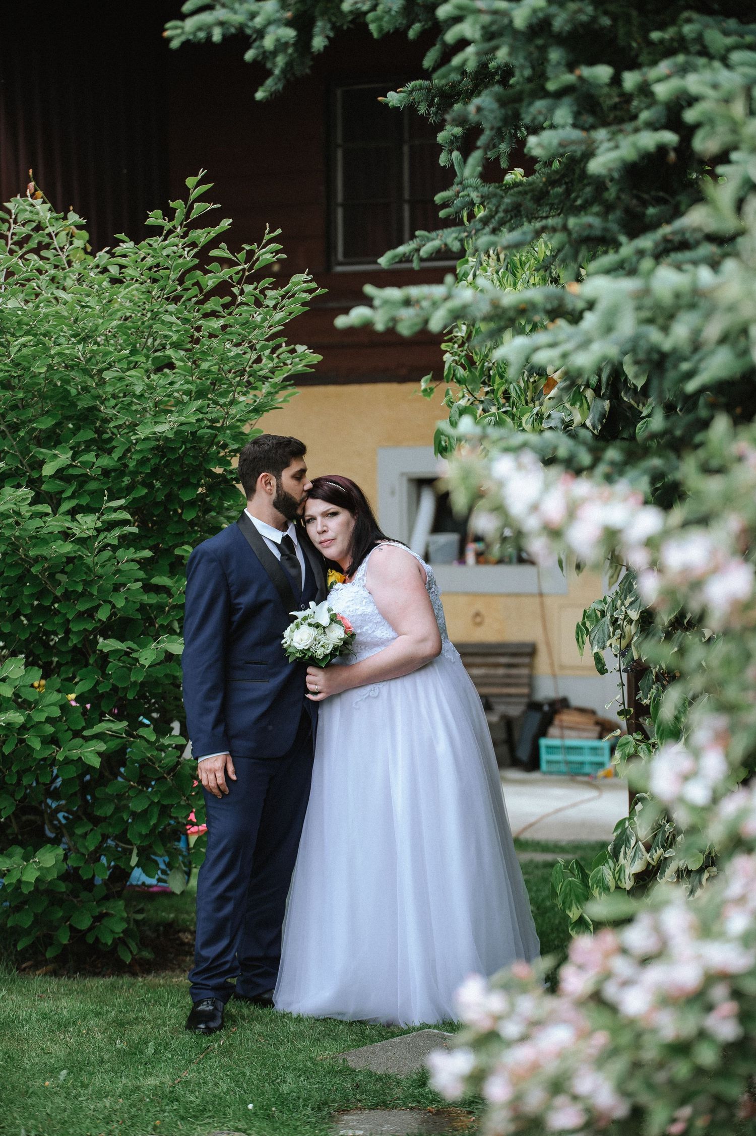 A romantic wedding portrait of a couple surrounded by flowering trees and greenery.