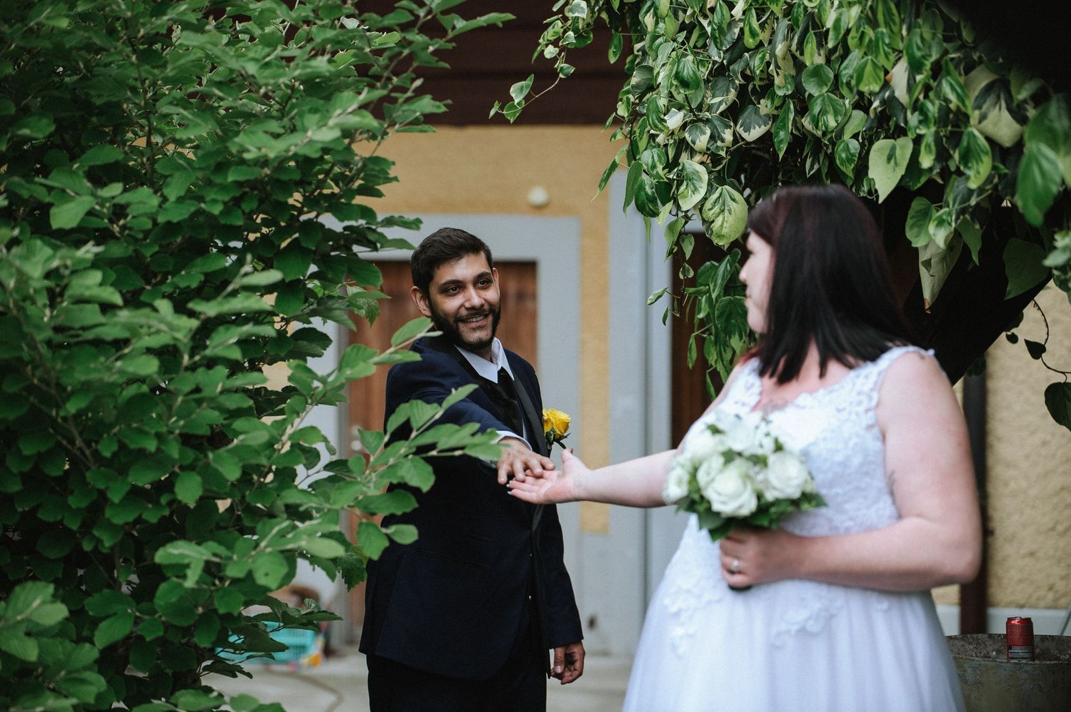 A couple shares a romantic moment in front of lush greenery at their wedding celebration.