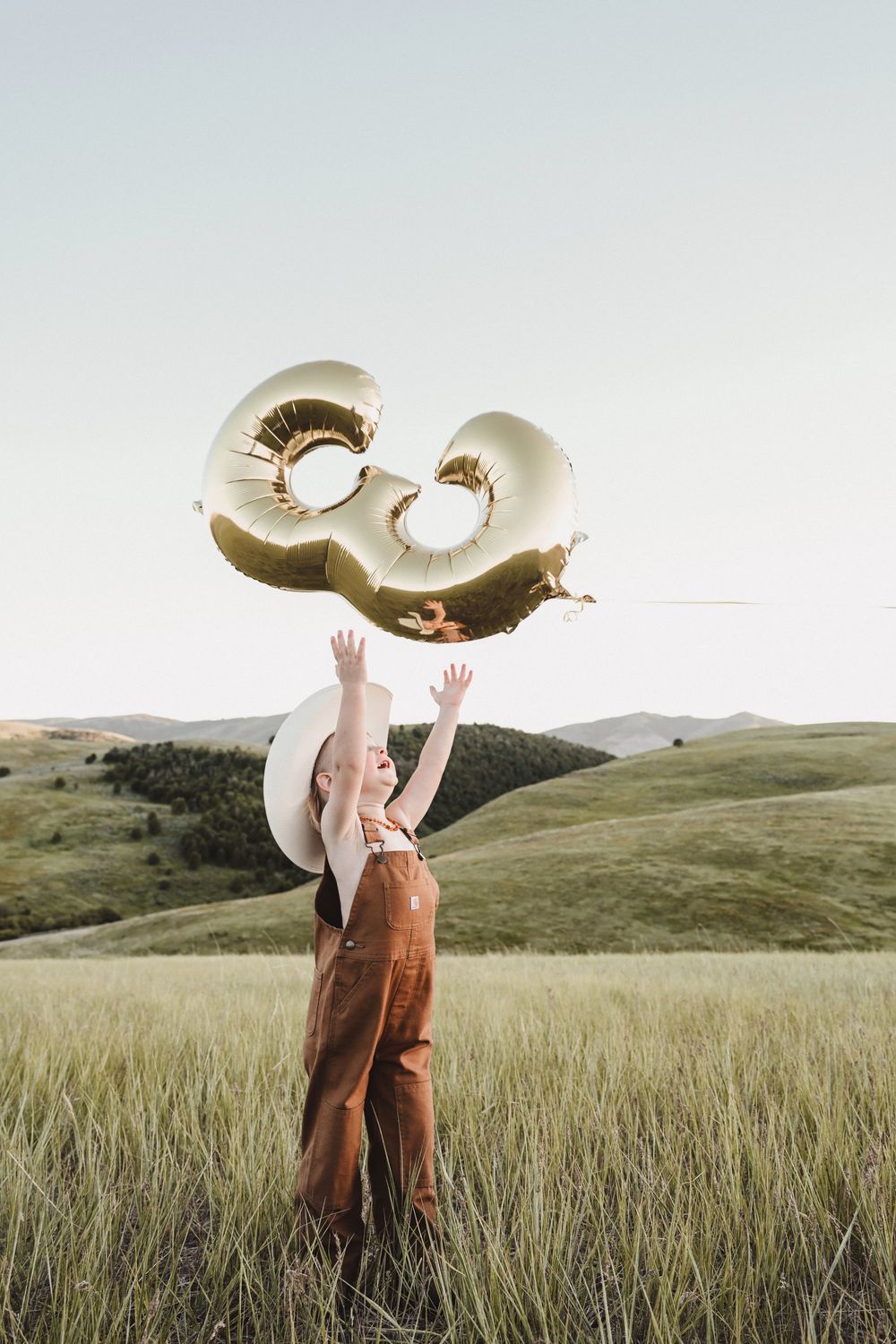 Figure holding large metallic balloon numbers in a grassy field during golden hour.