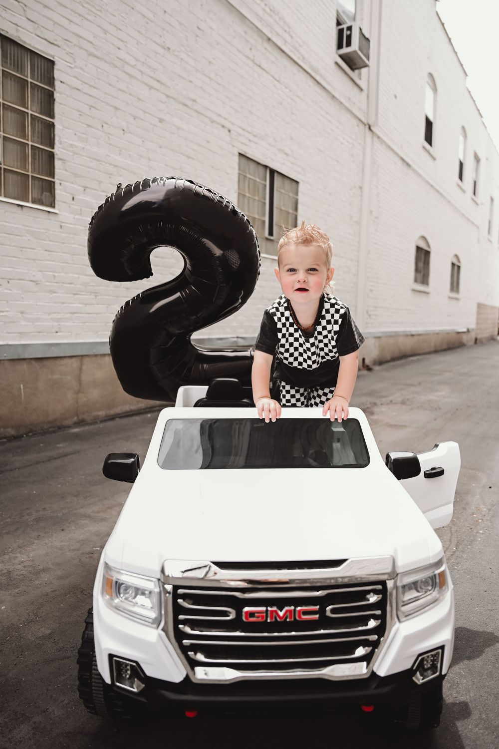 Toy white GMC truck with black balloon staged against white brick wall.