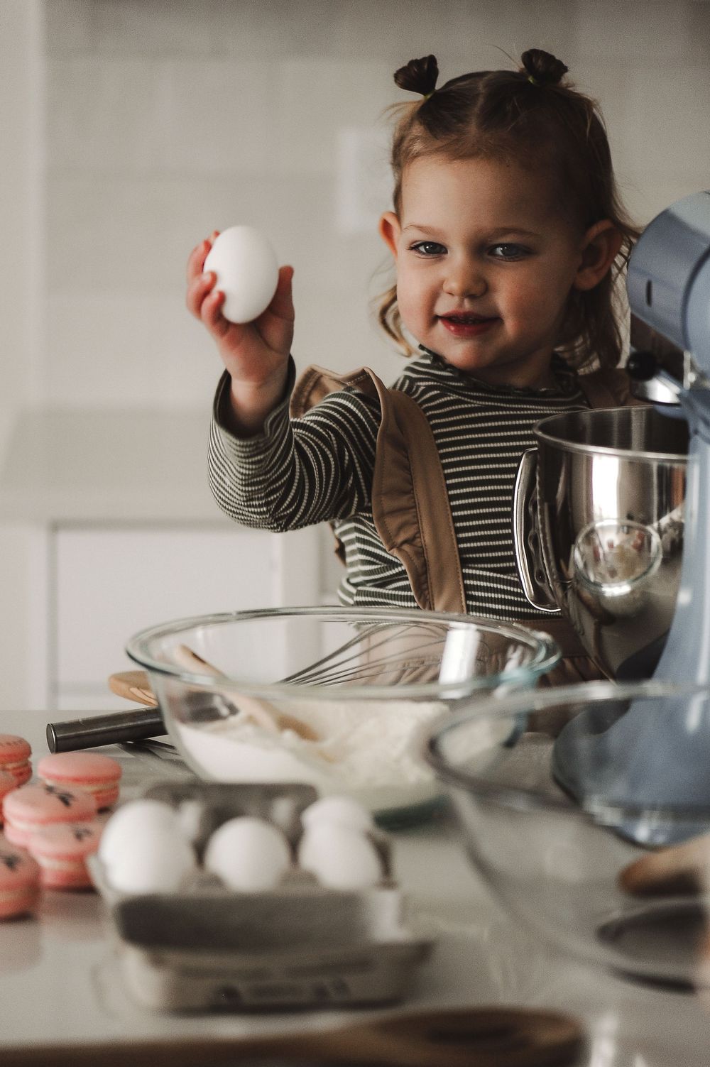 Child helping with baking ingredients at kitchen counter with mixing bowls.