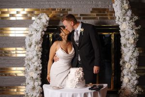 Wedding ceremony couple sharing intimate kiss at altar decorated with white floral arches and modern lighting.
