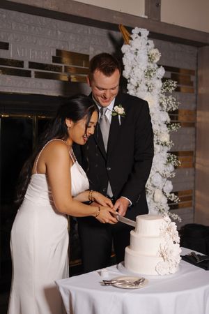 A couple shares a joyful moment cutting their elegant white wedding cake together at their reception.