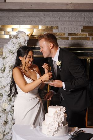 Newlyweds share a joyful moment while cutting into their elegant white textured wedding cake.