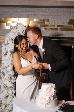 A joyful wedding moment captured as newlyweds share a laugh while cutting their elegant white floral cake.