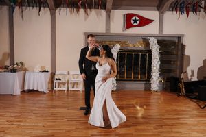 A couple shares a romantic dance in an elegant ballroom setting with natural wood floors and white decor.