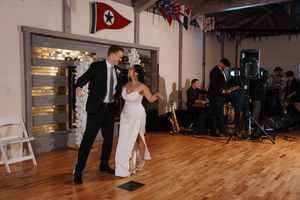 A couple dances together on a wooden floor during their wedding reception with decorative flags visible in the background.