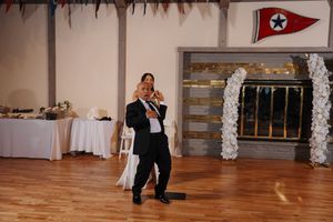 Dance partners glide gracefully across a wooden floor with a pennant flag visible on the wall behind them.