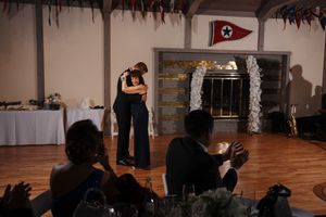 Two dancers share an intimate moment on a dance floor while guests watch and take photos during an evening celebration.