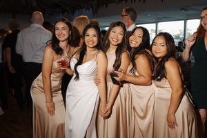 A group of women wearing champagne-colored bridesmaid dresses pose together at a wedding celebration.