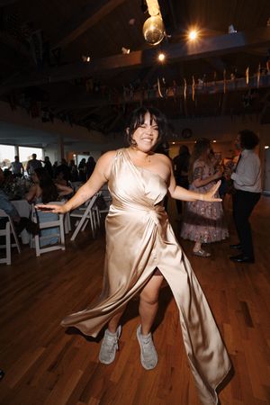 A person in a champagne-colored dress dances enthusiastically on a wooden dance floor at a party venue.