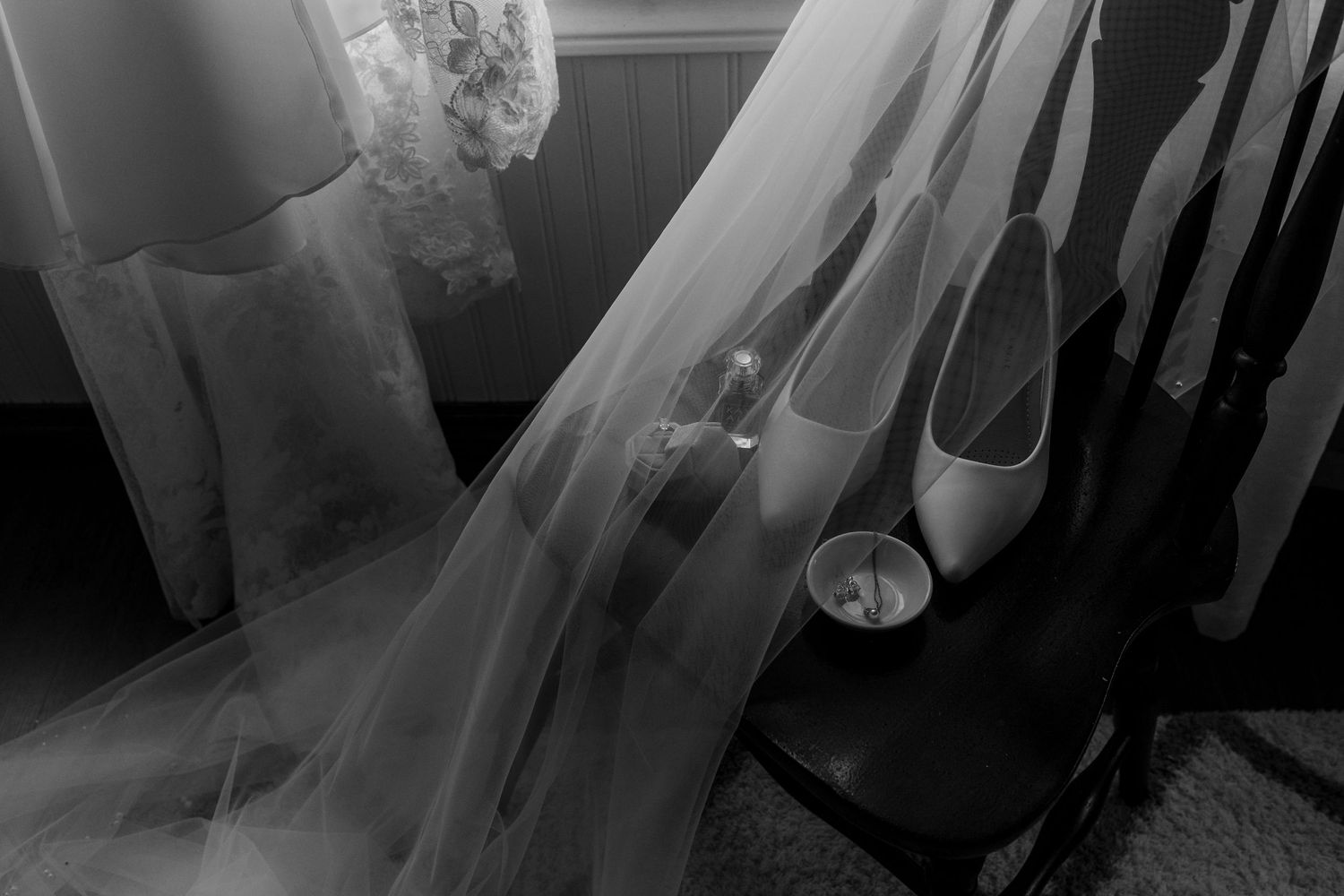 A wedding veil draped over elegant white bridal shoes arranged in black and white photography.