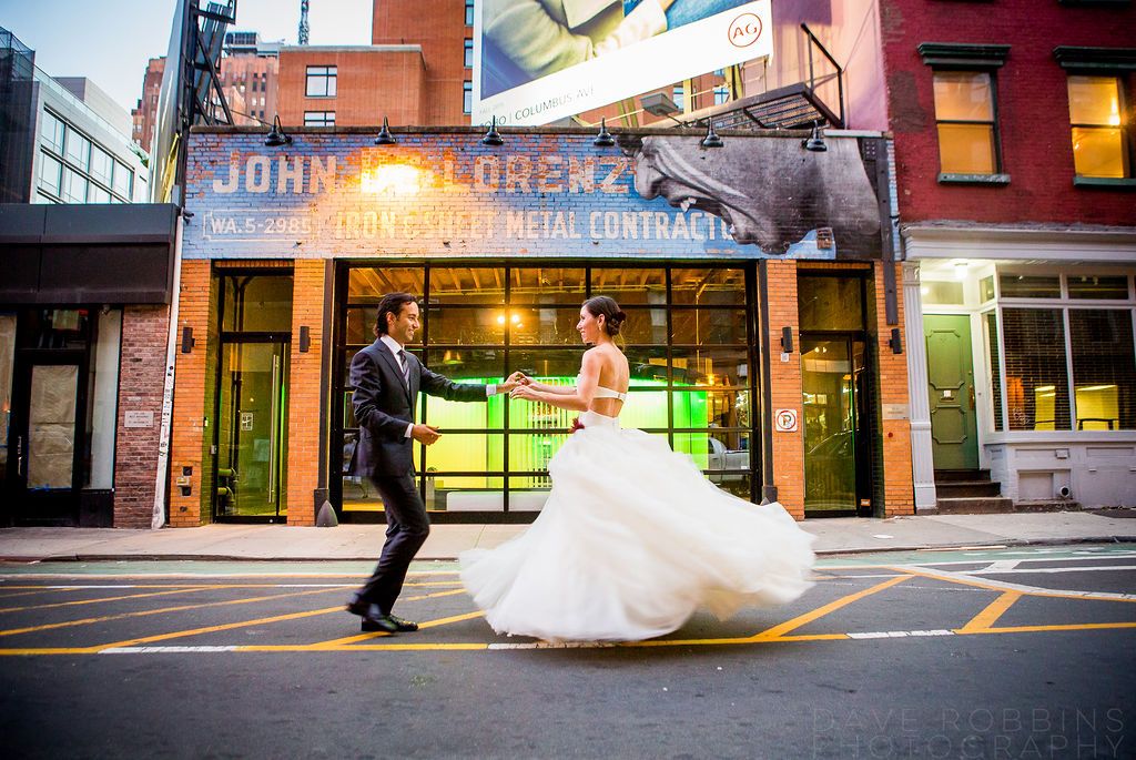 A couple embraces against a red brick wall while onlookers rest nearby on an urban street.