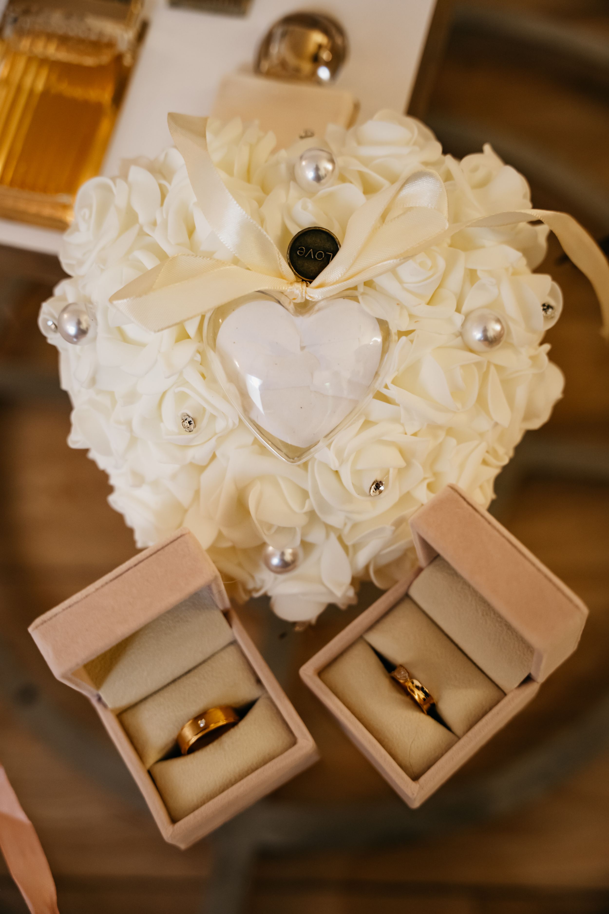 Three elegant beige ring boxes displayed with ornate white floral decorations and crystals atop each box.
