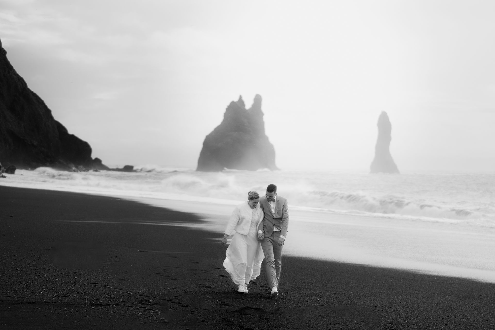 Couple walking together in the wind on Reyjnisfjara black sand beach.