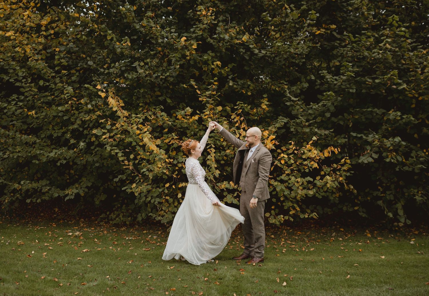 A wedding couple shares romantic moments in an autumn outdoor garden setting with golden leaves in the background.