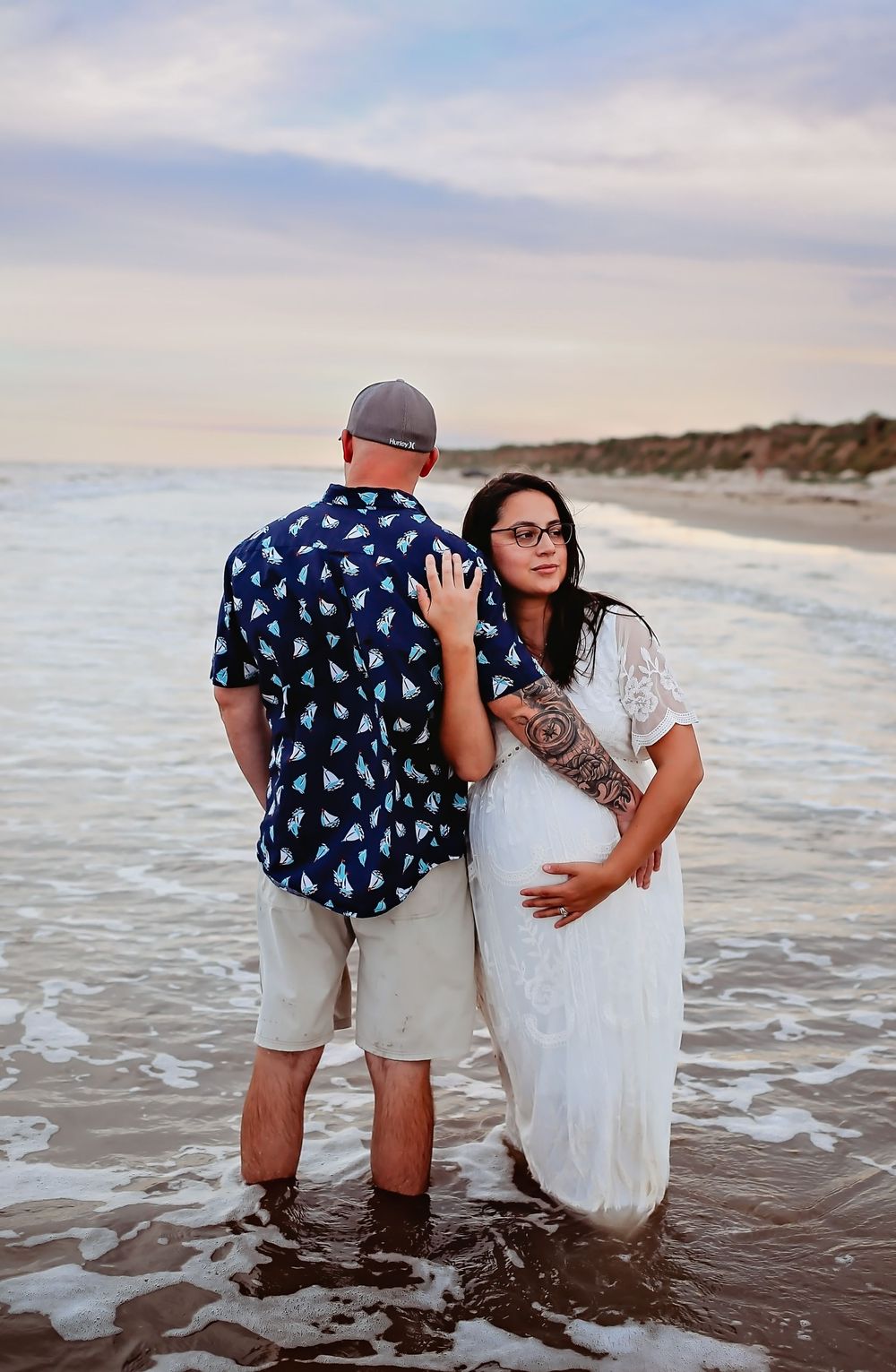 Husband and wife holding hands walking on the beach during maternity session