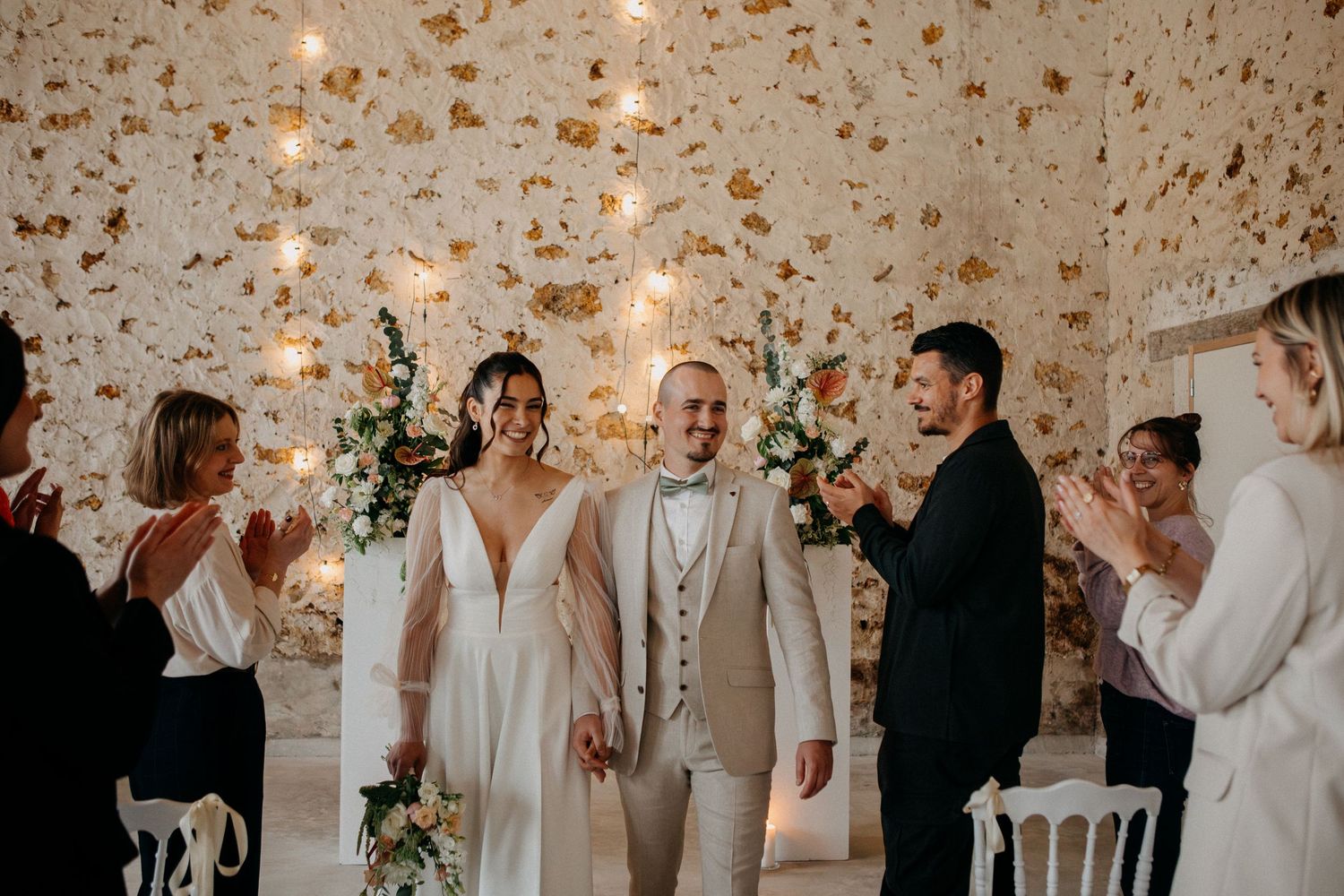 Joyful bride and groom walking down the aisle as guests celebrate with applause at a rustic wedding venue.