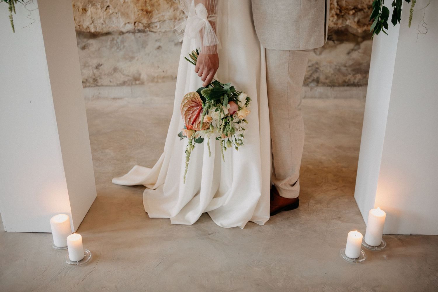 Close-up of bride and groom standing together with a bridal bouquet and white candles on the floor.