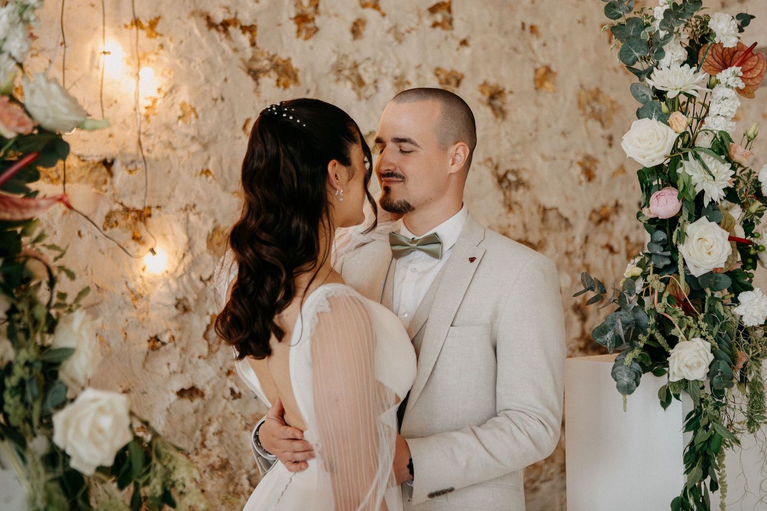 Bride and groom sharing a romantic moment about to kiss beneath a floral arch at their wedding ceremony.