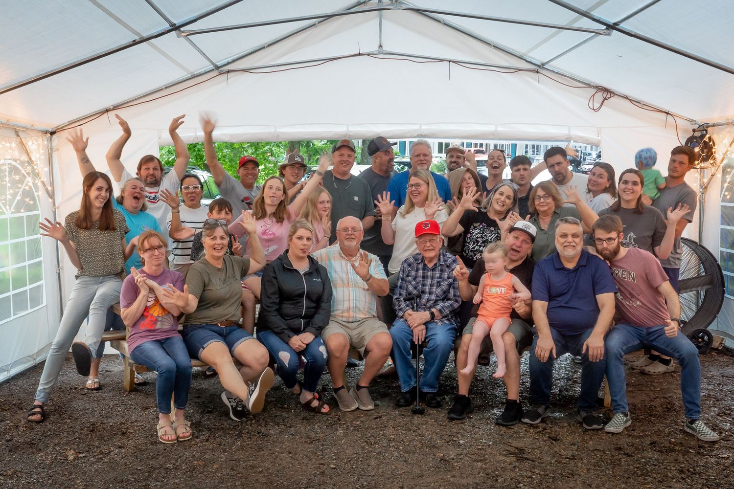 A large group photo of people gathered under a white tent at an outdoor event.