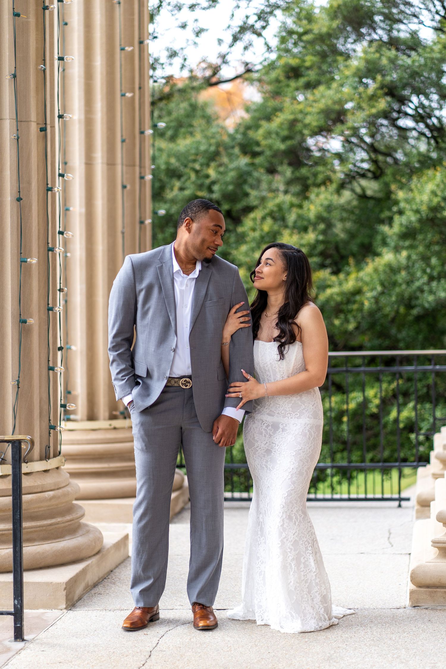 A couple in wedding attire shares a romantic moment between elegant stone columns on their special day.