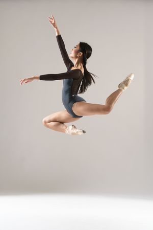 Dancer in black leotard executes powerful leap against light background.