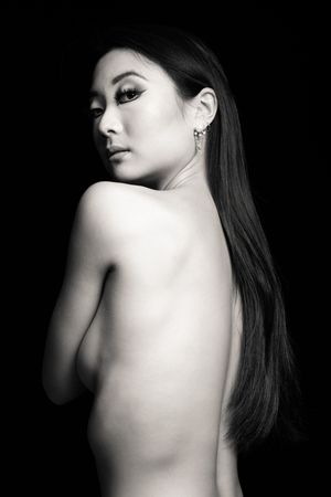 Dramatic black and white portrait showing bare shoulders and long dark hair.
