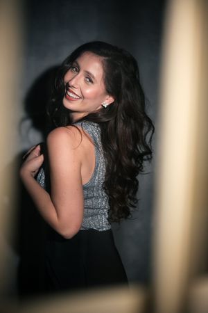 Portrait of woman in sparkly top smiling over shoulder in dramatic lighting between columns.